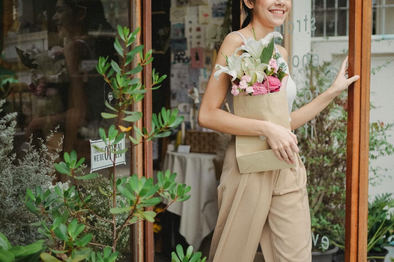Smiling woman carrying floral bouquet outside a charming flower shop.