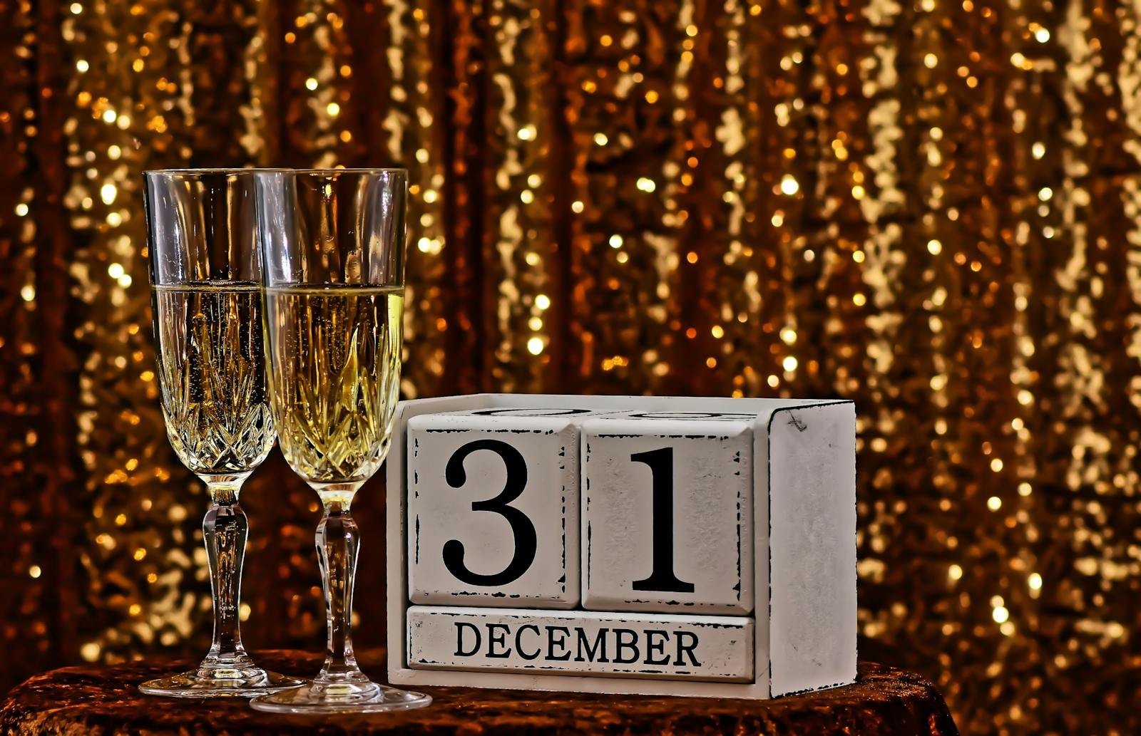 Two glasses of champagne with calendar blocks set to December 31 against a glittering gold background.